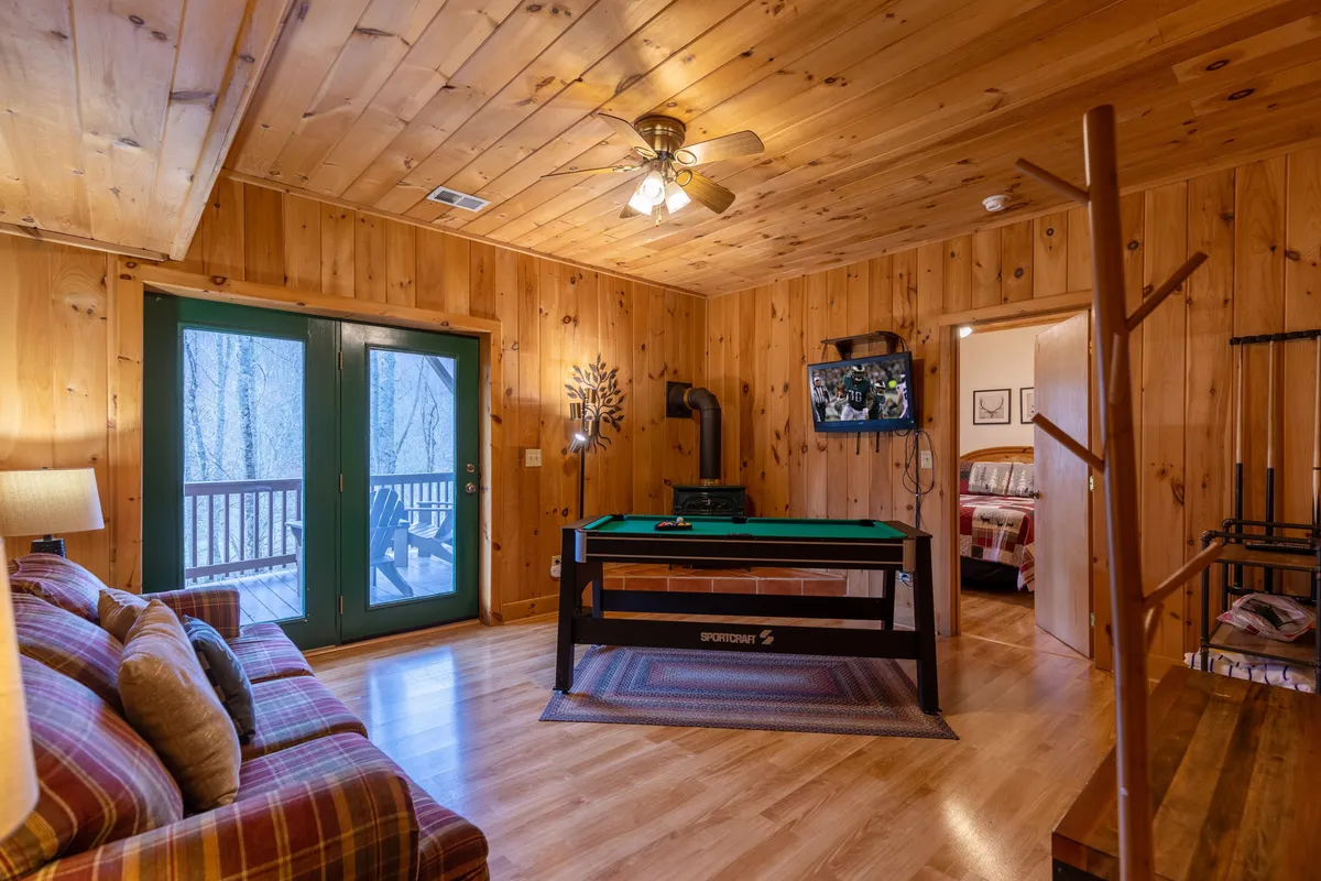 A lower-level rec room highlighted by a stylish pool table, comfortable sofa seating, large windows with serene views, and warm wooden walls. The space is clearly set up for both games and lounging, capturing a fun, inviting vibe suitable for teens or late-night hangouts.