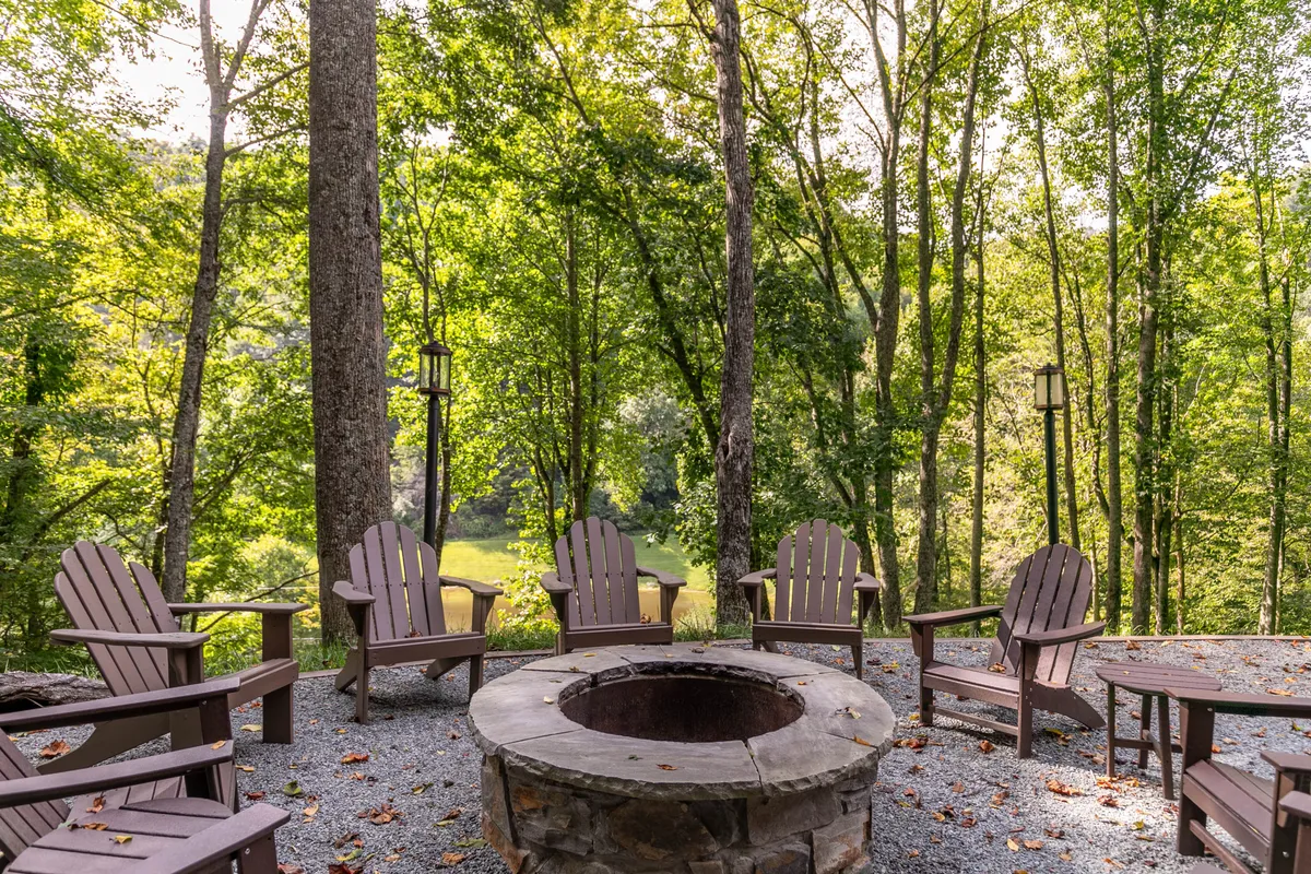 An inviting fire pit area is surrounded by Adirondack chairs and lamp posts, set against the backdrop of tall trees. The communal space is perfect for storytelling, stargazing, and relaxing after days exploring Boone and local attractions.