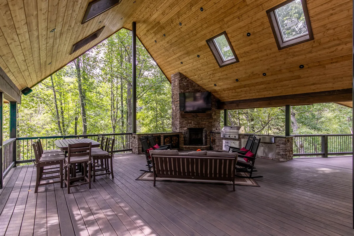 A covered porch and outdoor seating area with a wooden ceiling, skylights, a stone fireplace, and a large dining table. The inviting setup encourages outdoor dining and relaxation, seamlessly connecting the indoor living spaces to the scenic outdoors.