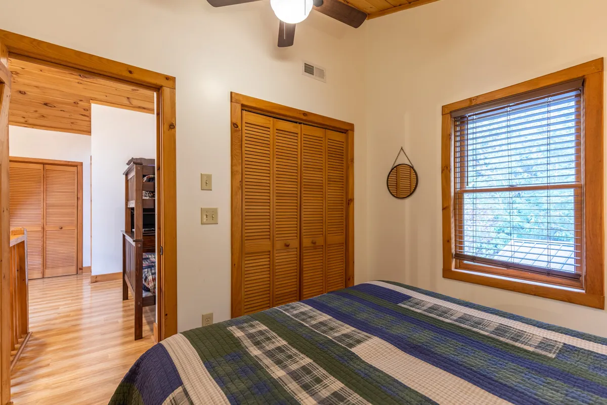 A warm, restful queen bedroom featuring a bed with a patterned quilt, wooden closet doors, and a window with blinds. The space exudes comfort and privacy, ideal for grandparents, couples, or friends.