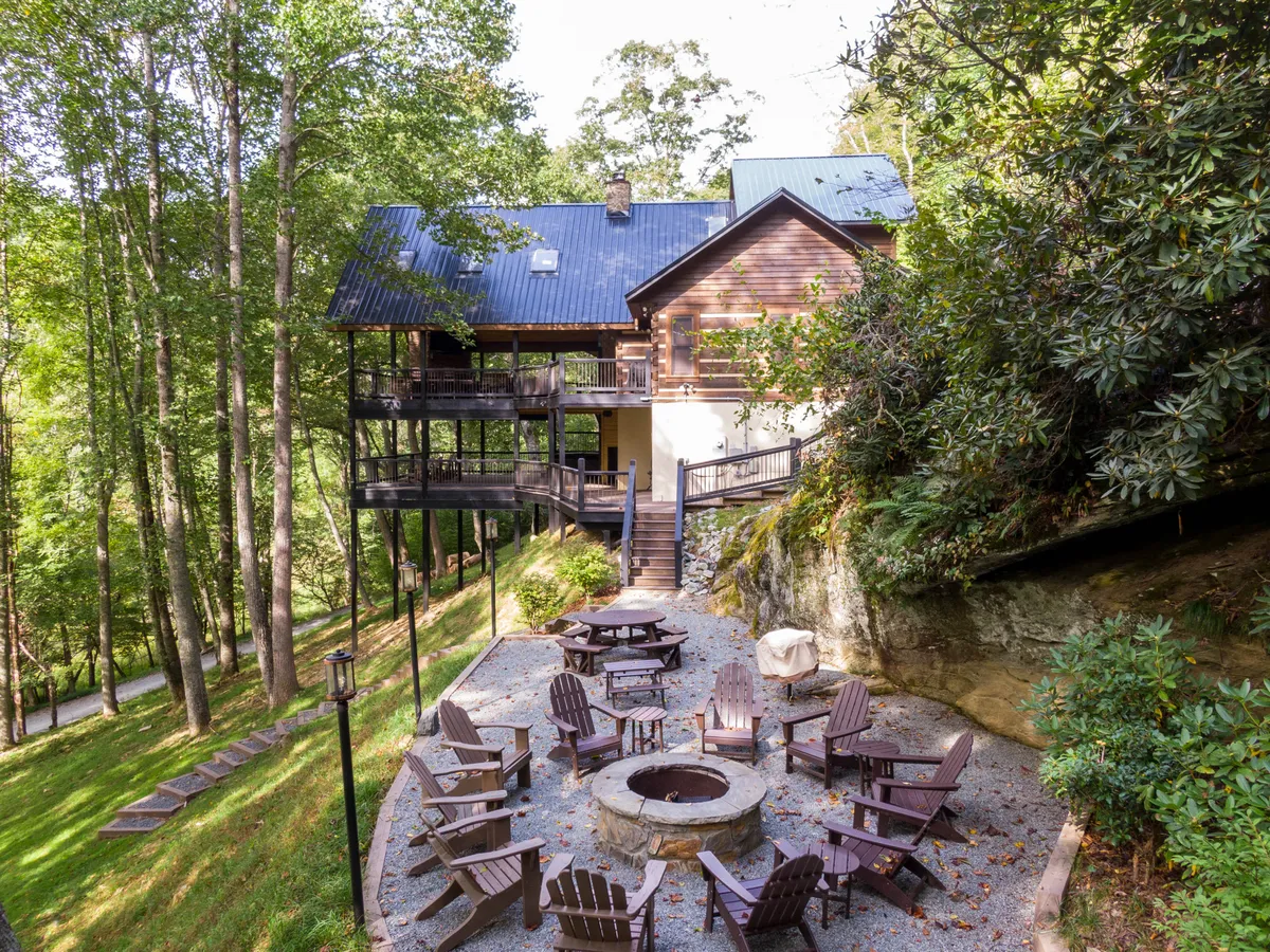 The wooden deck is framed by Adirondack chairs encircling a fire pit, all nestled among tall trees. The space invites socializing, relaxing after a day of adventure, or gathering under the stars for fireside chats.