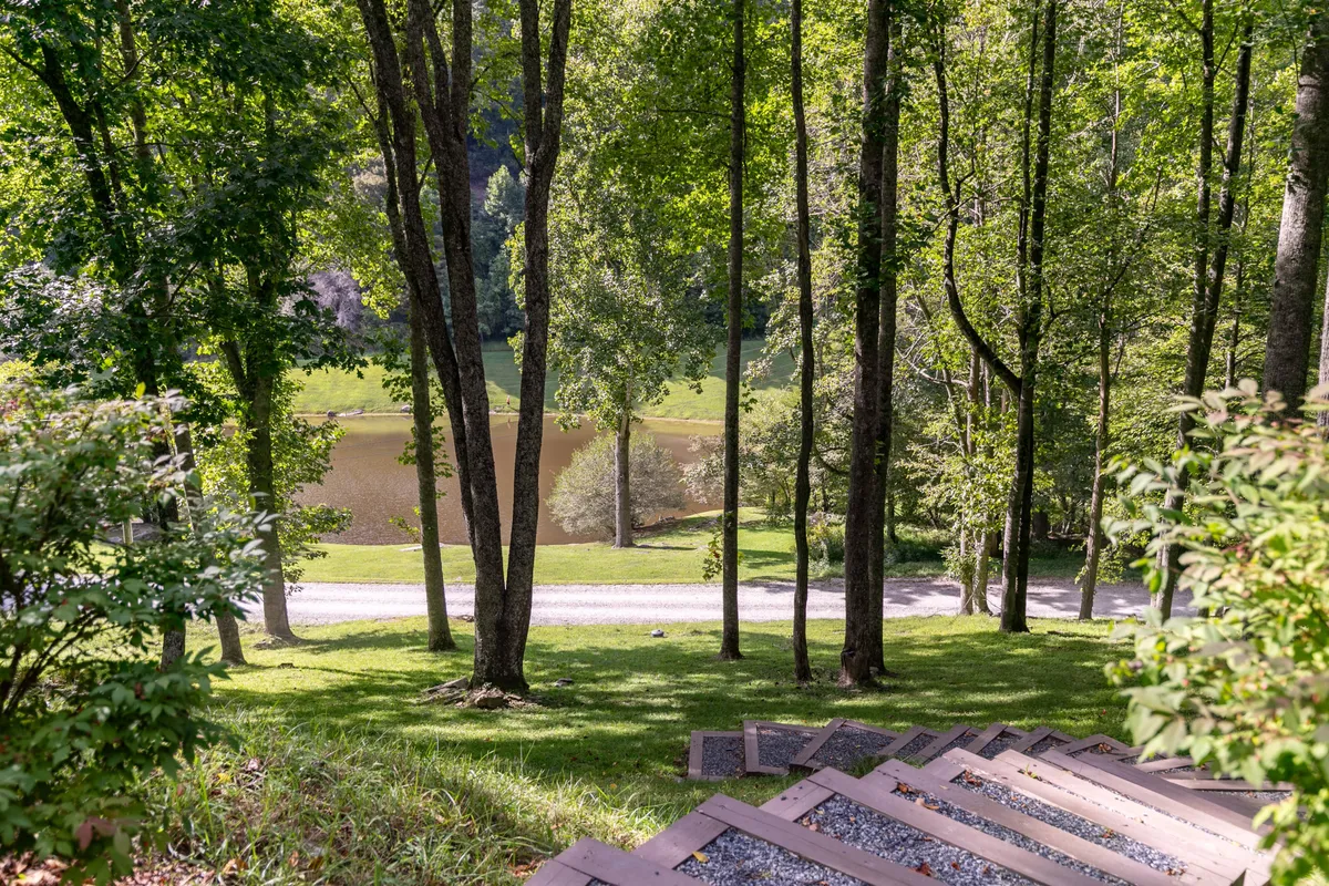 A serene view down a staircase leading through the forest to a reflective lake, framed by trees and natural landscape. The peaceful scene invites exploration and highlights immediate access to walking trails and lakefront activities.