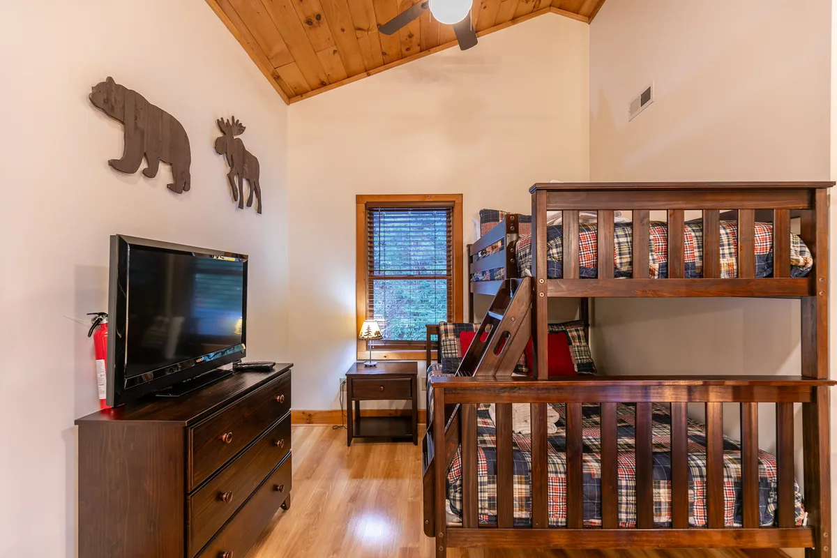 A cozy loft space with a twin-over-full bunk bed, television, wooden decor, and a window that lets in ample natural light. The room feels playful and inviting, suitable for kids or teens seeking a fun, flexible space.