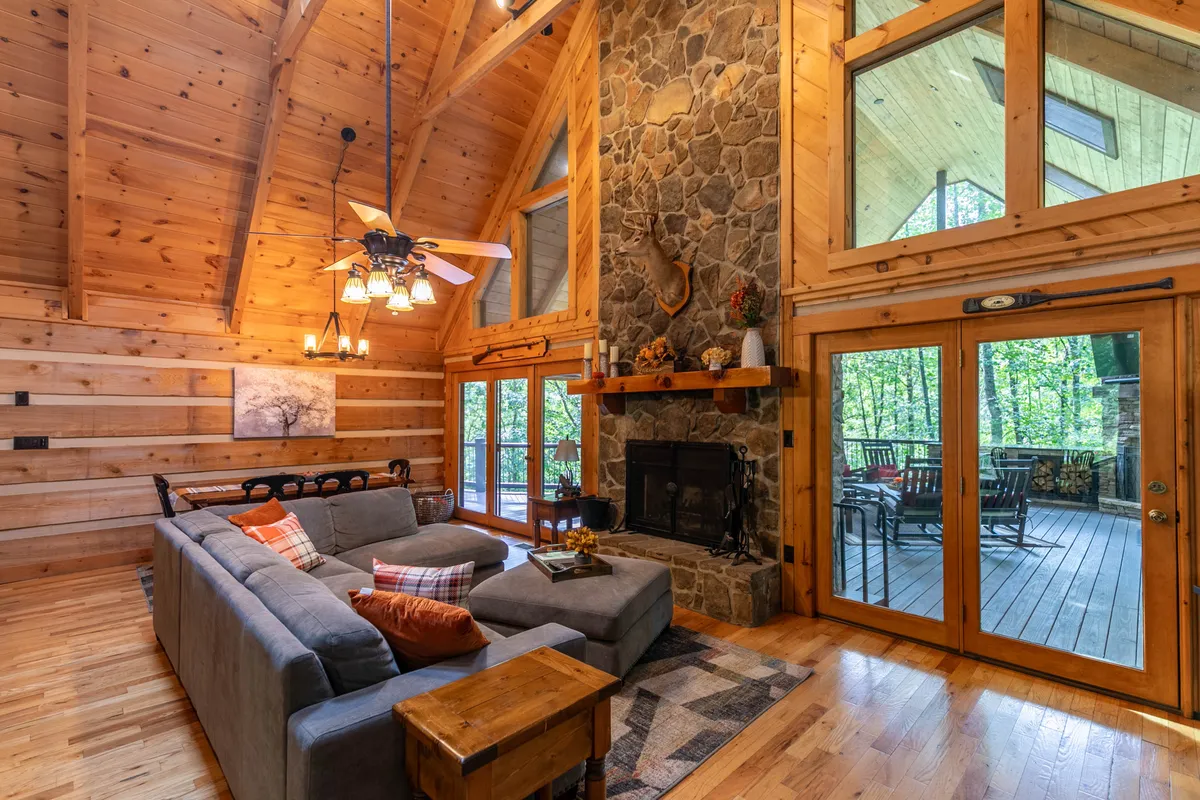 A spacious, warm family room featuring a stone fireplace, large windows that flood the space with natural light, a plush sectional sofa, and wood-paneled ceilings. The setting is perfect for family gatherings, movie nights, or game sessions in a relaxed, inviting atmosphere.