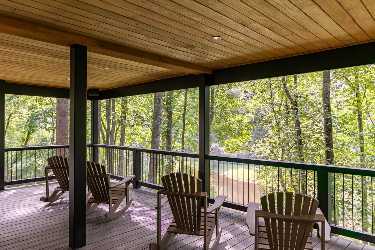 A tranquil wooden deck furnished with Adirondack chairs, surrounded by lush green foliage and offering a scenic view of the mountains. The outdoor setting is inviting, with direct access to nature and space for relaxing, socializing, or simply enjoying the fresh mountain air.