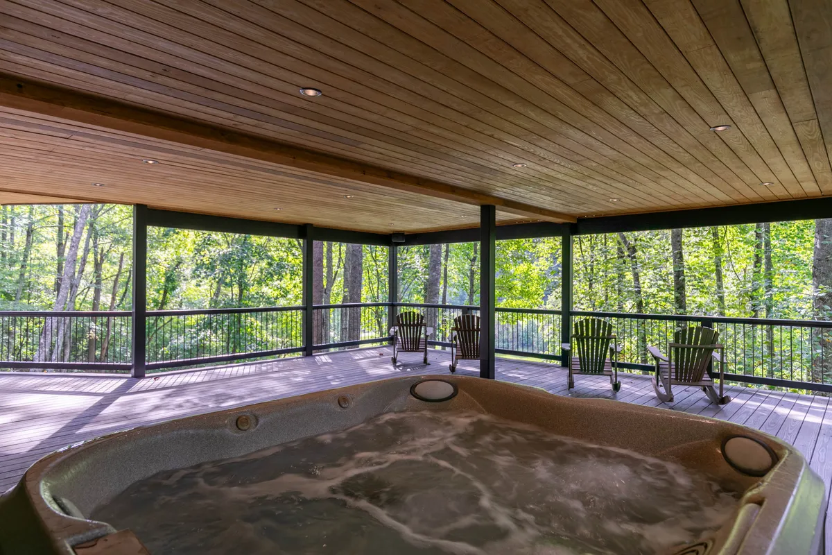 A serene hot tub scene on a wooden deck, surrounded by lush nature. The hot tub sits at the edge of the deck, offering sweeping views of the outdoors. The peaceful atmosphere suggests both morning coffee moments and evening relaxation, with plenty of space for socializing or soaking in solitude.